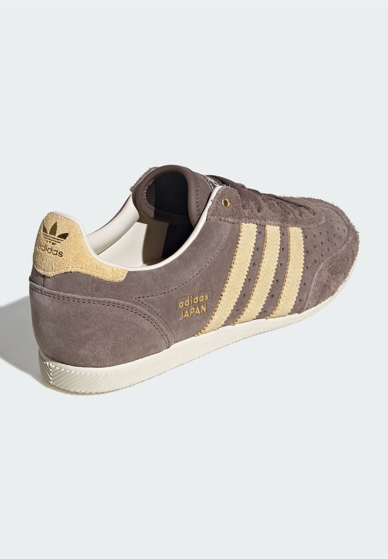 Adidas Japan-sneakers med mörkbrun mockauppdel, beige detaljer och tre ränder. Har guldfärgad branding och texturerad yttersula.