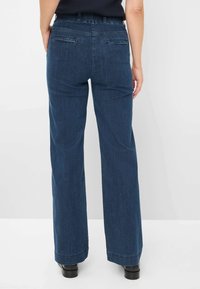 Donkerblauwe wijde jeans met een gladde textuur, voorzien van twee achterzakken en een getailleerde taille. De zoomafwerkingen zijn schoon en niet rafelig.