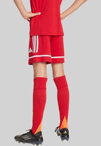 Maillot de sport rouge et shorts avec des rayures blanches, accompagnés de chaussettes rouges avec des accents orange et des crampons noirs. Texture lisse, design sportif.