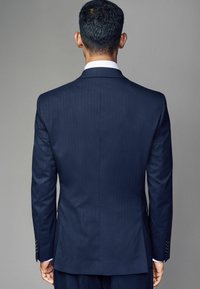 Marineblaues, gestreiftes Sakkos mit glatter Textur. Mit Revers und geknöpften Manschetten; von hinten vor einem grauen Hintergrund sichtbar.