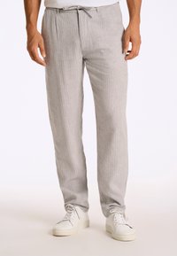 Pantalons texturés gris clair avec une taille à cordon, présentant des rayures verticales et une coupe droite, associés à des baskets blanches.