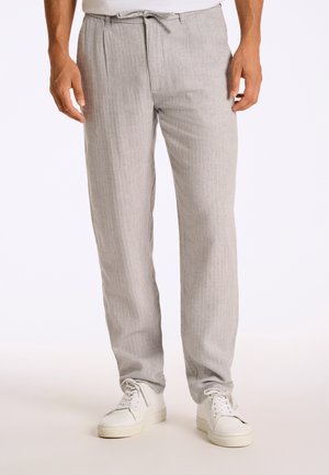 Pantalons texturés gris clair avec une taille à cordon, présentant des rayures verticales et une coupe droite, associés à des baskets blanches.