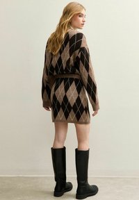 Sweter z dzianiny w czarno-brązowy wzór argyle, w połączeniu z dopasowaną spódnicą i czarnymi kolanówkami, wyeksponowany na neutralnym tle.