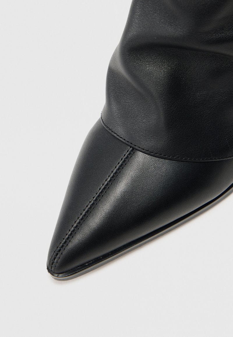 Schwarzer Leder-Stiefel mit spitzem Zeh und weichem, gerafftem Obermaterial. Merkmale sind die glatte Textur und dezente Steppnähte entlang der Naht.