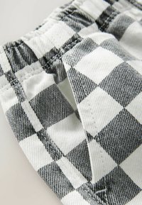 Tissu à carreaux noir et blanc avec une finition douce et texturée. Taille élastique avec des détails de couture visibles. Motif affiché de manière proéminente.