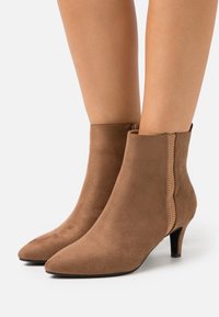 Bottes courtes en daim brun avec un bout pointu, un petit talon kitten bas et un détail de panneau latéral texturé.