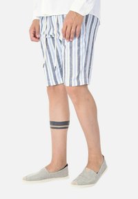 Pantaloni corti in lino a righe blu chiaro e bianchi con vita elastica e coulisse. Abbinati a scarpe grigie slip-on.