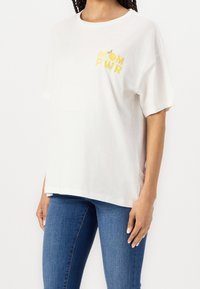 Vit bomullströja med oversize-passform, korta ärmar och gul broderad "MOM PWR" design med en tecknad limeaccent.