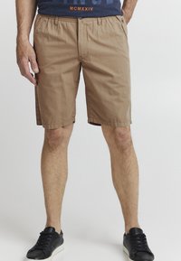 Kaki shorts laget av lett materiale, med avslappet passform, sidelommer og rett kant. Kombinert med svarte sneakers.