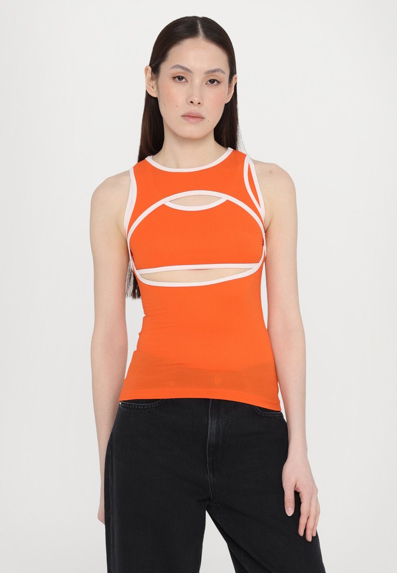 Canotta arancione attillata con dettagli bianchi, caratterizzata da un design a taglio circolare. Tessuto elasticizzato con una texture liscia, abbinata a jeans neri.