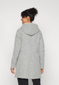 Gray, textured coat with a hood, featuring long sleeves and a relaxed fit, visible stitching and side pockets, styled with a clean back.