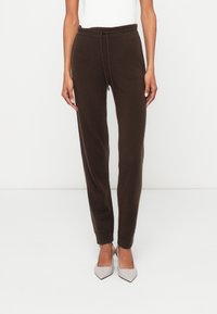 Brązowe dzianinowe spodnie dresowe z regulowanym paskiem w talii, ściągaczami przy kostkach i zwężającym się krojem. W połączeniu z jasnoszarymi butami ze spiczastym noskiem.