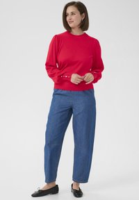 Red knit sweater with long puffed sleeves and button detail at cuffs, paired with blue denim wide-leg pants and black flat shoes.