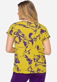 Top amarillo de manga corta con un patrón de patitos morados. El diseño es holgado, con un escote redondeado y una textura suave.