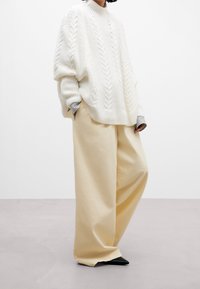 Bílý pletený oversized svetr s copánkovým vzorem, doplněný krémovými kalhotami s širokými nohavicemi. Černé špičaté baleríny dotvářejí outfit.