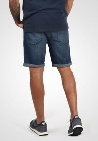 Mørkeblå denimshorts med optrukne bukseben, to baglommer og en klassisk pasform, parret med grå sneakers, der viser Nike-logoet.