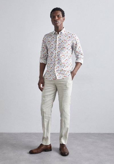 Chemise à boutons à motif floral en blanc, pantalon en lin beige clair et chaussures en cuir marron. Le design comprend des manches retroussées et un col.