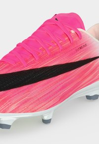 Lyserød fodboldstøvle med sort Nike-swoosh, snørebånd og hvid sål med grå knopper, mærket "Flyweave" på siden.