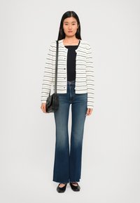 Cardigan bianco a maglia con righe nere orizzontali, abbinato a jeans blu a zampa d'elefante e una borsa a tracolla nera. Scarpe nere flat completano il look.