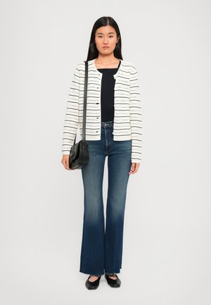 White knit cardigan with horizontal black stripes, paired with flared blue jeans and a black crossbody bag. Flat black shoes complete the look.
