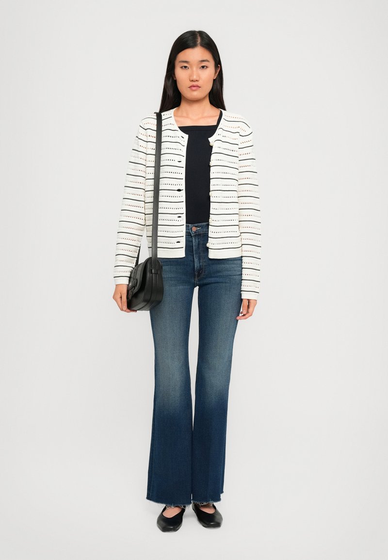 Cardigan bianco a maglia con righe nere orizzontali, abbinato a jeans blu a zampa d'elefante e una borsa a tracolla nera. Scarpe nere flat completano il look.