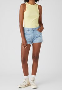 Žluté žebrované tílko, modré džínové šortky s třepeným lemem a bílé tenisky s vysokým klenutím se kontrastními ponožkami. Jednoduchý a ležérní outfit.