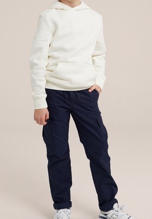 Valkoinen hupullinen collegepaita edentaskulla, parina laivastonsiniset cargo-housut sivutaskuilla, yhditetty valkoisten lenkkitossujen kanssa.