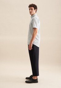 Lichtblauw en witte geruite kortekoope blouse, gecombineerd met marineblauwe broeken en zwarte veterschoenen, gepresenteerd tegen een neutrale achtergrond.