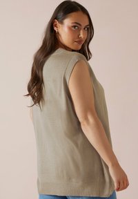 Beige ärmlös stickad topp med en rundad halsringning och ribbade kanter. Slät textur med en avslappnad passform, parat med ljusblå jeans.