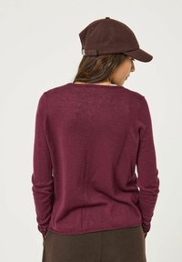 Haut à manches longues bourgogne avec un col rond et une coupe décontractée, associé à une casquette marron foncé avec un détail de bouton à l'arrière.