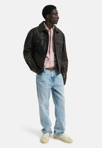 Mörkbrun läderjacka, ljusrosa randig skjorta, ljusblå jeans, krämfärgade sneakers. Jackan har tryckknappar och två bröstfickor.