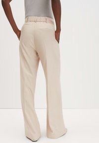 Wijdvallende broek in beige stof, met een geplooide elastische tailleband en een achterzak, die een gladde, zachte textuur biedt.
