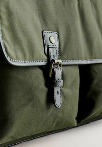 Olíva zöld vászontáska, hajtóka zárással, bőrszíjjal és fémbújtatóval, varrott részletekkel és texturált felülettel.