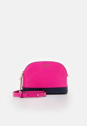 Kleine kuppelförmige Umhängetasche in leuchtendem Pink mit schwarzem Boden, verstellbarem Riemen, goldener Kettendetail und goldenem Kate Spade New York Logo.