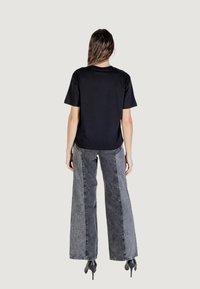 Camiseta negra de manga corta combinada con jeans de pierna ancha en tonos de gris, con paneles laterales en contraste, y zapatos de tacón negros.