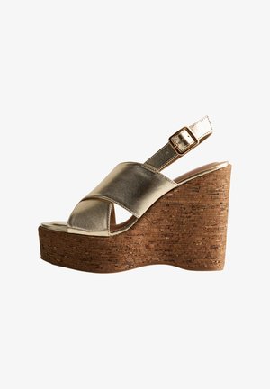 Gouden metallic wedge sandaal met een kurken plateau. Heeft een kruislings bandendesign en een verstelbare gesp. Gladde textuur.