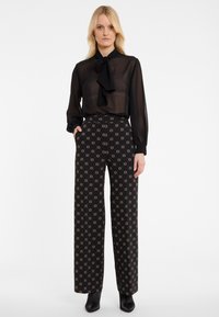 Black sheer blouse with bow tie detail, paired with high-waisted black pants featuring a gold circular pattern. Smooth texture, tailored fit.