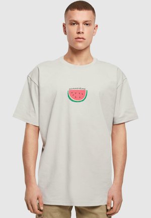Lys beige bomulds t-shirt med et vandmelonmotiv med grønne accenter og teksten "sommer" over. Løs pasform, korte ærmer.