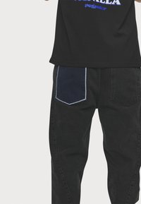 Camiseta de algodón negra con texto azul y pantalones de mezclilla negros con un bolsillo parche azul en la parte posterior, destacando texturas y colores contrastantes.