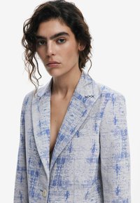 Ljust blå och vit blazer med ett strukturerat mönster, enkel knappknäppning, uppvikt krage och dekorativ sömmar på kragen.