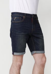 Shorts de mezclilla oscura con un diseño ajustado, puños enrollados en mezclilla clara y costuras en contraste. Incluye bolsillos frontales y cierre de botón.