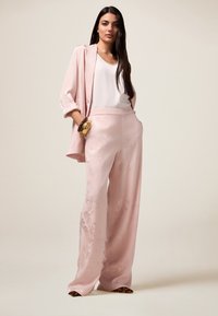 Light pink satin suit featuring a relaxed blazer and wide-leg trousers, adorned with subtle floral patterns and a smooth, shiny texture.