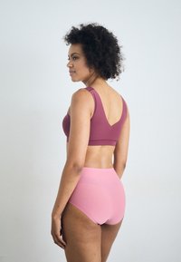 Lila Sport-BH mit breiten Trägern und V-Rücken, kombiniert mit hochtaillierten rosa Shorts. Beide Teile haben eine glatte Textur.