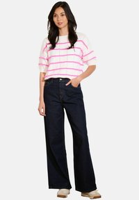 Bílý svetr s růžovými pruhy, krátké rukávy; vysoké pasové, široké džínové kalhoty tmavé barvy; tenisky dotváří celý outfit.