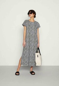 Vestido maxi com mangas curtas, apresentando um padrão de folhas em preto e branco. Fenda lateral e tecido suave. Combinado com uma mala de mão em creme.