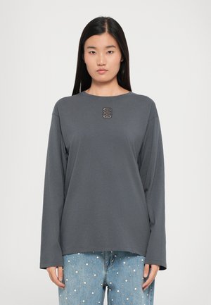 Maglietta grigia a maniche lunghe in tessuto morbido con scollatura rotonda. Presenta un dettaglio decorativo sul petto e una vestibilità comoda. Abbinata a denim.