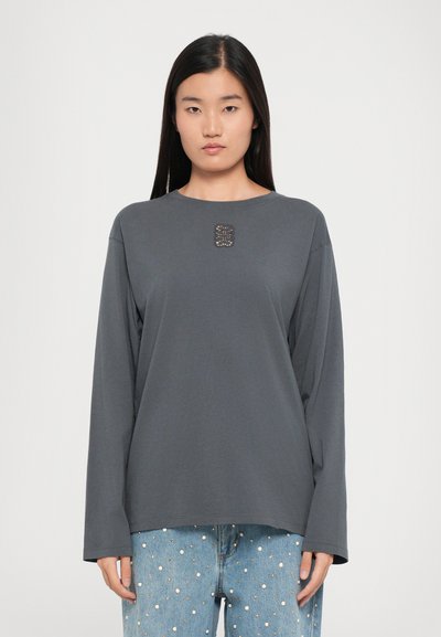 Langærmet grå skjorte i blødt stof med rund halsudskæring. Har en dekorativ accent ved brystet og en afslappet pasform. Kombination med denim.