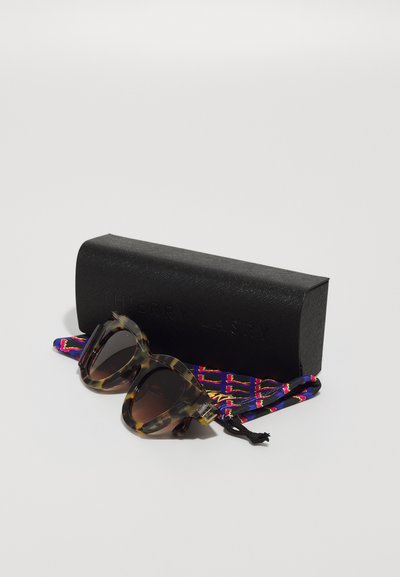 Tortoiseshell sunglasses with dark lenses, accompanied by a colorful patterned strap and a matte black case embossed with "THIERRY LASRY."