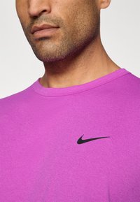 Lila sportpóló, puha anyagból készült, kerek nyakkivágással és fekete Nike pipa logóval a bal mellen.