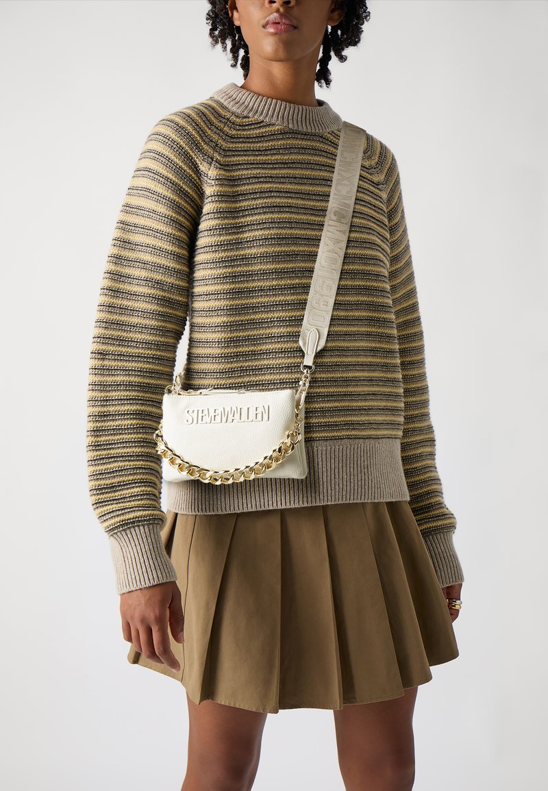 Braun-beige gestreifter Pullover, beige plissierter Rock und weiße Leder-Crossbody-Tasche mit goldener Kette und geprägtem Logo-Riemen.